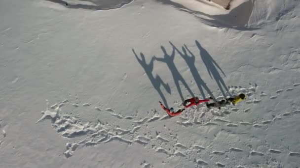 Vier Reisende tanzen und zeigen verschiedene lustige Figuren, die einen großen Schatten auf dem weißen Schnee reflektieren. Luftaufnahme großer Schatten. — Stockvideo