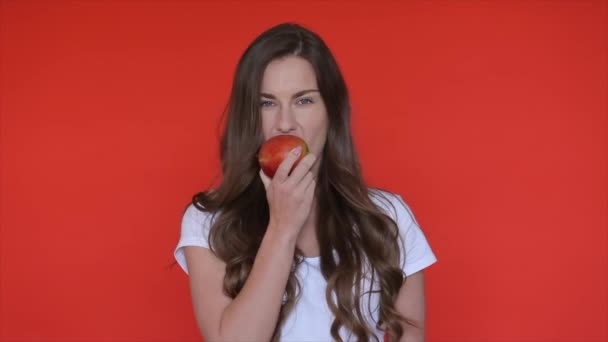 女性はリンゴを食べる 女の子はリンゴの果物をかむ 人の美しさの肖像 歯科医療 女性は赤いスタジオでリンゴを楽しむ 健康的な栄養食品 健康的な果物を食べる女性 — ストック動画