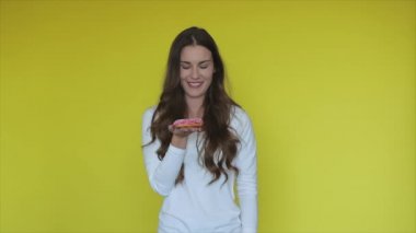 Sarı stüdyoda pembe çörek tutan mutlu kadın. Tatlı tatlısı olan mutlu insan. Gülümseyen kız çöreğin tadını çıkarıyor. Lezzetli diyet. Pastalı donutla mutlu insan.