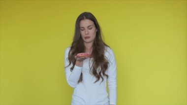 Sarı arka planda donut tutan yorgun bir kadın. Kadınlar tatlı çörek ister ama yemezler. Esmer modelin portresi tatlı olarak acı çekiyor. Sağlıklı bir yaşam tarzı. Tatlı yiyeceksiz kadın diyeti