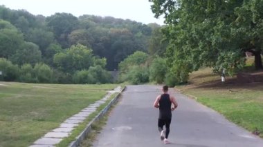 Koşu yapan adam parkın açık hava manzarasında koşuyor. Summerpark 'taki koşan adamın arka görüntüsü. Siyah spor giyim maratonunda sağlıklı bir koşucu. Dayanıklılık sabahı egzersizi. Aktif atlet antrenmanı kardiyo
