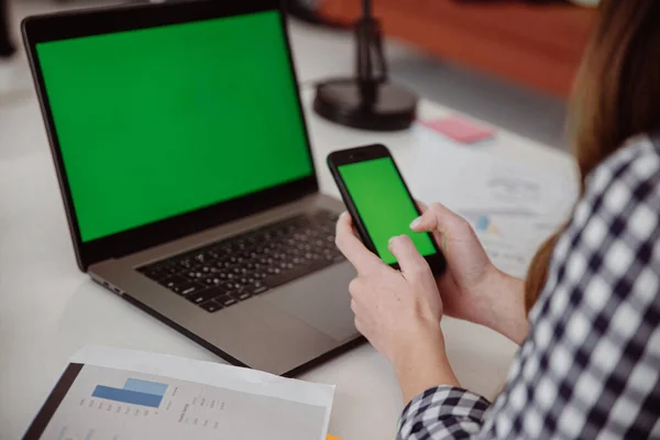 Рука жінки тримає мобільний телефон з зеленим екраном. Зелений екран на мобільному пристрої ноутбука Ліцензійні Стокові Зображення