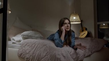 Yatak odasında telefonla konuşan bir kadın. Pijamalı sıradan bir kız cep telefonuyla konuşuyor.