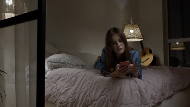 Nő görgetett telefon a hálószobában éjszaka. Modern lány használ szerkentyűt alvás előtt — Stock videók