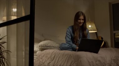 Yatak odasında dizüstü bilgisayar kullanan mutlu bir kadın. Neşeli kadın bilgisayara bakıyor