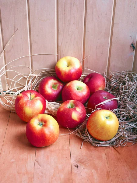 Bright red and yellow apples are stored in hay on a wooden surface