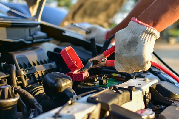 Technician\'s hand connects the car battery charger with electricity via jumper wires.