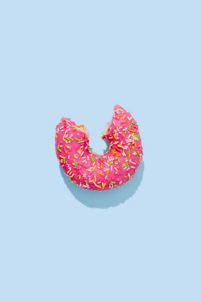 Bitten Donut in pink glaze with colorful sprinkles on a blue background