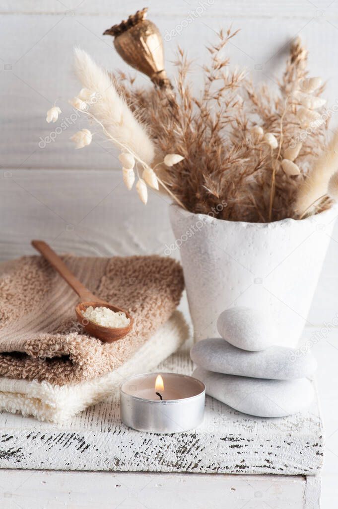 Beige lit aroma candle and golden dry flowers on rustic background. Spa arrangement with salt in monochrome style