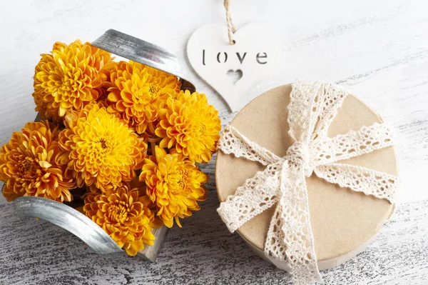 Orange flowers in box on rustic background. Greeting card with heart and kraft gift box