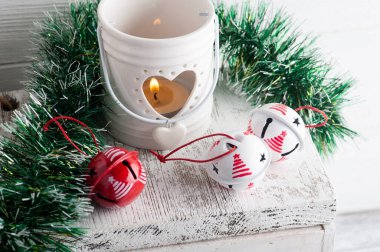 Kırmızı ve beyaz şıngırtılı Noel süslemesi ve beyaz kırsal arka planda mum.