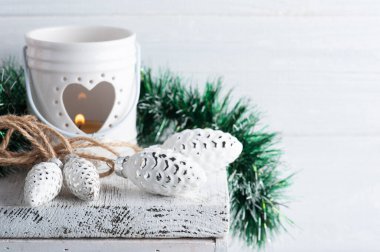 Oyuncak çam kozalaklarıyla Noel süslemesi ve beyaz köy arka planında mum yakmak. Karşılama için alanı kopyala