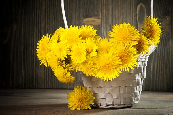 Dandelions in a basket on dark wooden background — Stock Photo, Image