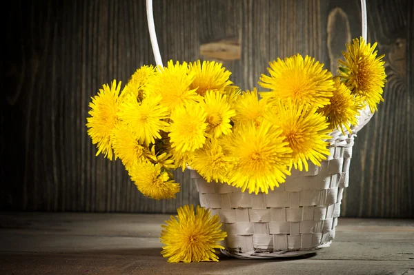 Dandelions koyu ahşap zemin üzerinde bir sepet içinde 