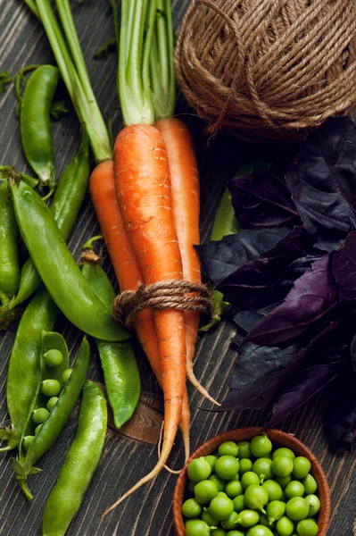 Zanahorias crudas, guisantes verdes y albahaca sobre mesa de madera —  Fotos de Stock