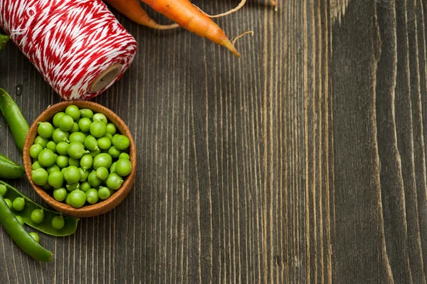 Zanahorias crudas, guisantes verdes y cordel rojo sobre mesa de madera —  Fotos de Stock