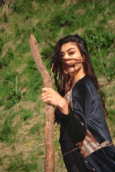 Frau im nationalen schwarzen Samtkleid mit einem Stock in der Hand und ausdrucksstarken Augen auf dem Hintergrund der Natur — Stockfoto