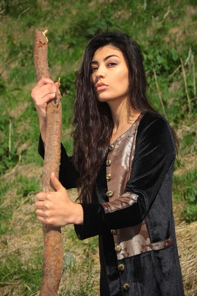 Frau im nationalen schwarzen Samtkleid mit einem Stock in der Hand und ausdrucksstarken Augen auf dem Hintergrund der Natur — Stockfoto