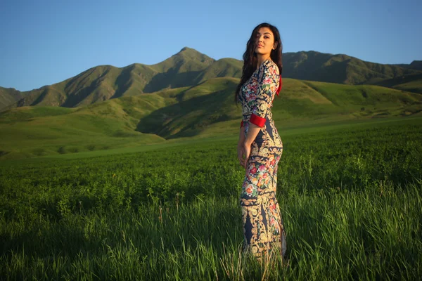 Mulher em platte ao pôr do sol em um campo em um fundo de montanhas — Fotografia de Stock