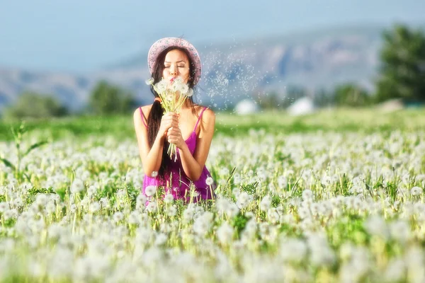 Modell im rosa Kleid auf einem Löwenzahnfeld mit Strohhut — Stockfoto