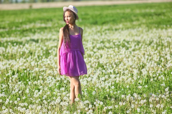 Modelo em um vestido rosa em um campo de dente de leão em um chapéu de palha — Fotografia de Stock