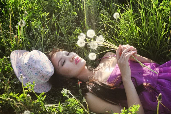 Modelo em um vestido rosa em um campo de dente de leão em um chapéu de palha — Fotografia de Stock