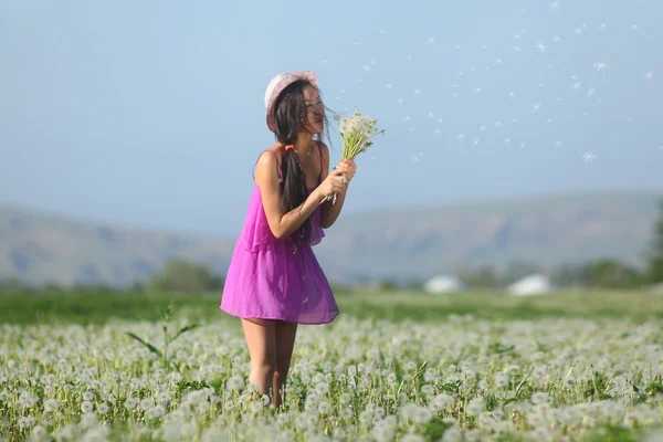 Modell im rosa Kleid auf einem Löwenzahnfeld mit Strohhut — Stockfoto