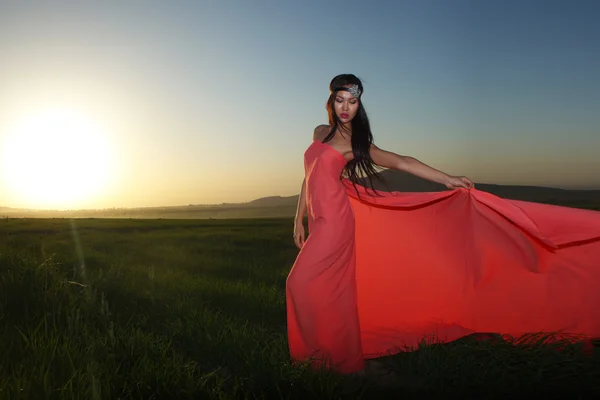 Model in rotem Kleid posiert bei Sonnenuntergang auf dem Feld — Stockfoto