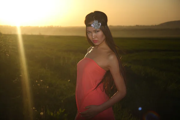 Model in rotem Kleid posiert bei Sonnenuntergang auf dem Feld — Stockfoto