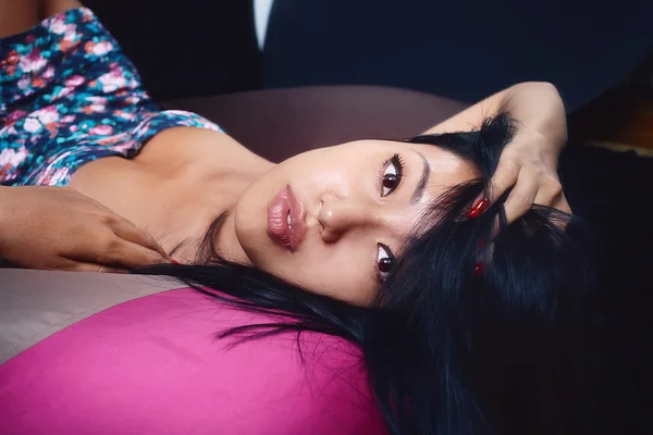 Charming woman in a floral blue dress posing relaxed lying on  bean bag on a black background — Stock Photo, Image