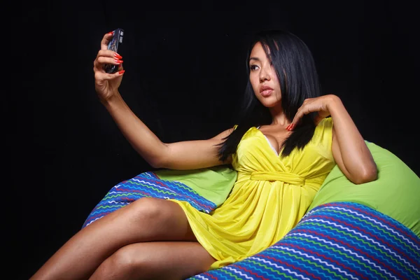 Elegant woman in a yellow dress posing lying on bean bag on a black background — Stock Photo, Image