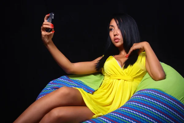 Elegant woman in a yellow dress posing lying on bean bag on a black background — Stock Photo, Image