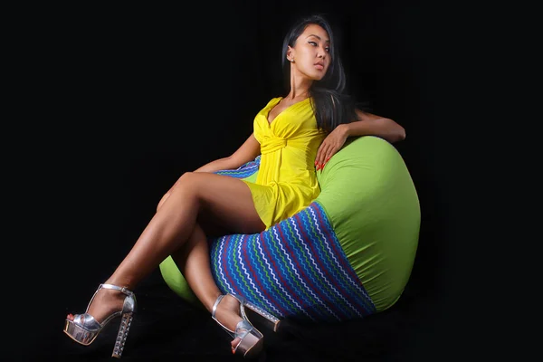 Elegant woman in a yellow dress posing lying on bean bag on a black background — Stock Photo, Image