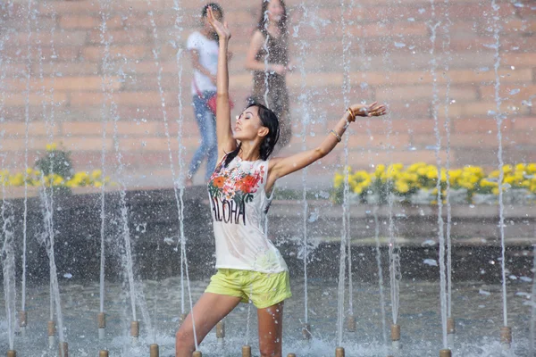 Cheerful girl dancing under jets of water in city fountain — Stock Photo, Image