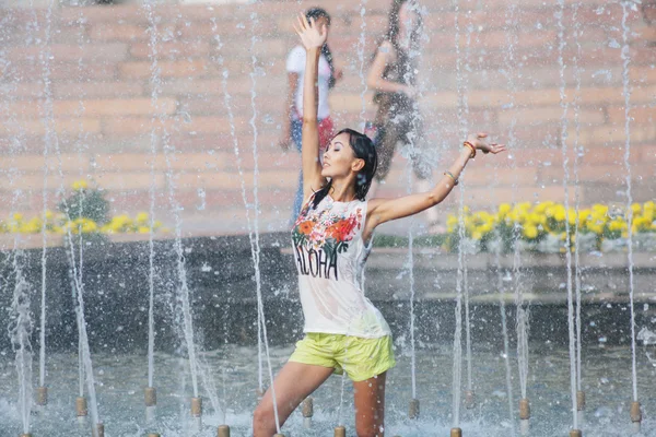 Cheerful girl dancing under jets of water in city fountain — Stock Photo, Image