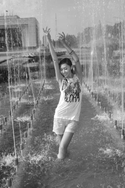 Cheerful girl dancing under jets of water in city fountain — Stock Photo, Image