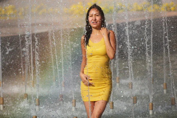 Chica en un vestido elegante con el pelo largo en gotitas de agua en la fuente de la ciudad — Foto de Stock