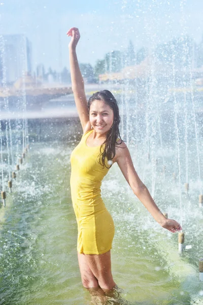 Fille dans une robe slinky avec les cheveux longs en gouttelettes d'eau dans la fontaine de la ville — Photo