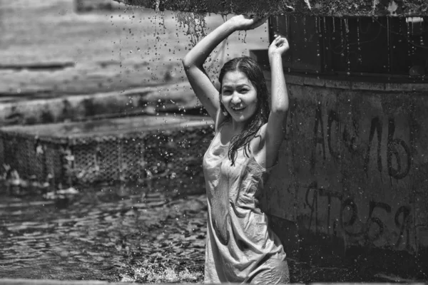 Menina em um vestido pegajoso com cabelos longos em gotas de água na fonte da cidade — Fotografia de Stock