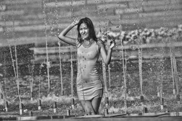 Chica en un vestido elegante con el pelo largo en gotitas de agua en la fuente de la ciudad —  Fotos de Stock