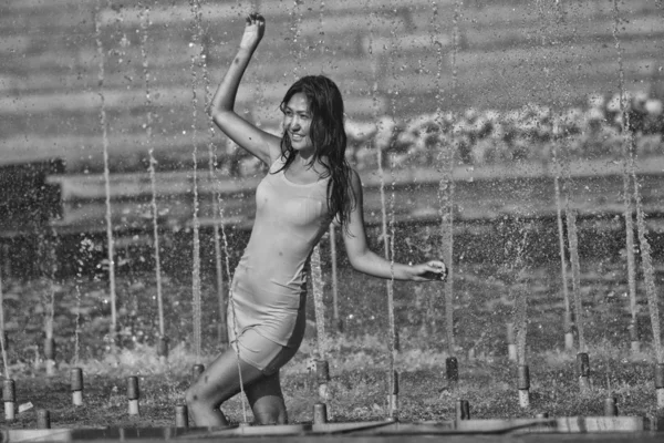 Chica en un vestido elegante con el pelo largo en gotitas de agua en la fuente de la ciudad —  Fotos de Stock