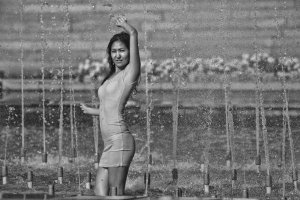 Girl in a slinky dress with long hair in water droplets in the city fountain — Stock Photo, Image