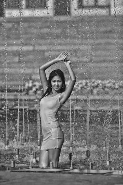 Girl in a slinky dress with long hair in water droplets in the city fountain — Stock Photo, Image