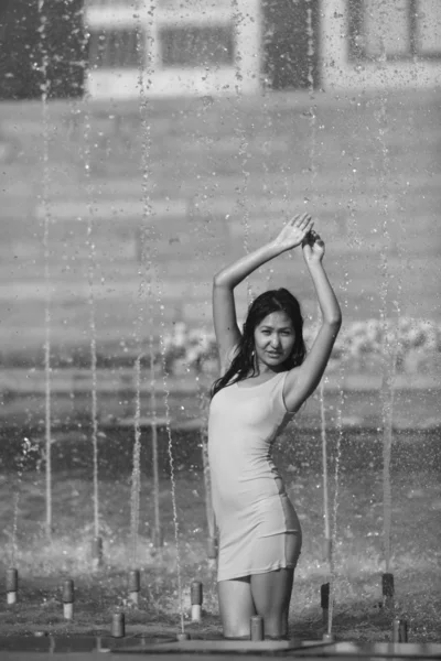 Chica en un vestido elegante con el pelo largo en gotitas de agua en la fuente de la ciudad —  Fotos de Stock