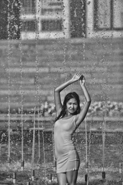 Ragazza in un abito slinky con i capelli lunghi in goccioline d'acqua nella fontana della città — Foto Stock