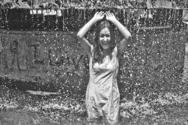 Menina em um vestido pegajoso com cabelos longos em gotas de água na fonte da cidade — Fotografia de Stock