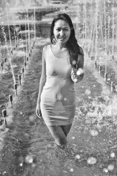 Girl in a slinky dress with long hair in water droplets in the city fountain — Stock Photo, Image