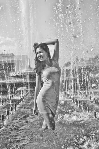 Chica en un vestido elegante con el pelo largo en gotitas de agua en la fuente de la ciudad —  Fotos de Stock