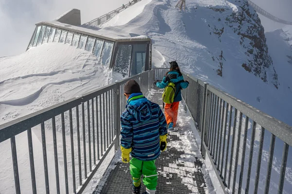 Back view of one boy and one girl walking on the bridge on the top of the mountain. Winter vacation with children in Alps. Glacier 3000, les Diablerets, Switzerland. Happy childhood.