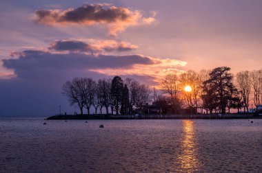 İsviçre, Lozan 'daki ağaçların ve bulutların olduğu gölün üzerinde gün batımı. Huzurlu sahne ve doğada güzellik.